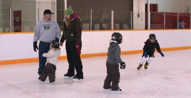 Two Adults and 3 Kids Skating on the Arena Ice